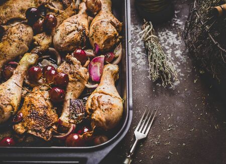 Close up of roasted chicken drumsticks with red onion and grapes on dark background.の写真素材
