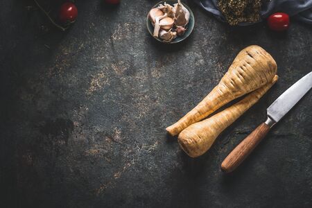 Food background with fresh parsnips roots on dark kitchen tables with knife. Top view. Vegetables cooking conceptの写真素材