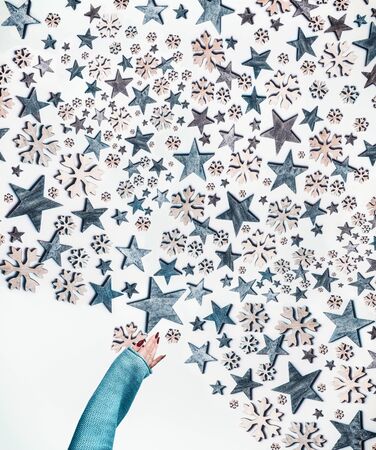 Female hand make Christmas stars and snowflakes pattern on white background. Top view. Creative holiday concept. Flat lay. White blue colors. Winter layoutの写真素材