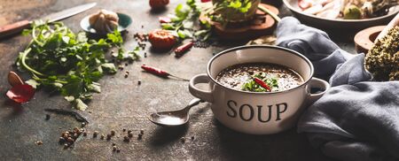 Bowl with lentil soup on rustic kitchen table  with spoon and various ingredients.
