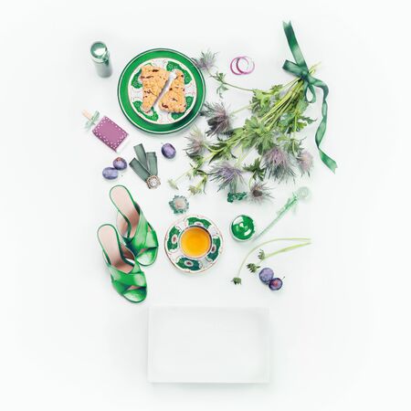 Female beauty flat lay with green high heels, flowers, cup of tea, cakes, cosmetics and blank white paper boxの写真素材