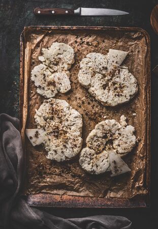 Vegan food cooking preparation. Cauliflower steaks on baking sheet with knife on rustic background. Top viewの写真素材