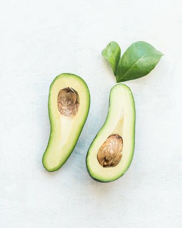 Avocado cut in half with green leaves on white tableの写真素材