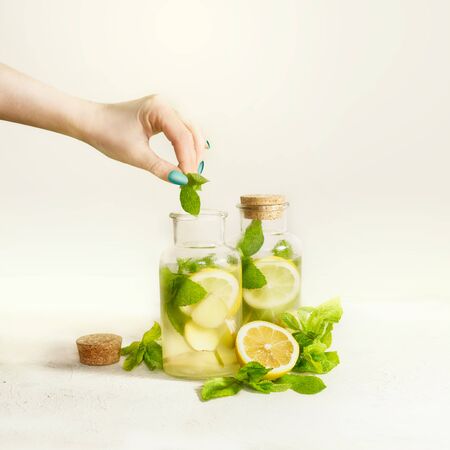 Female hand with green manicure making healthy drink lemonade in bottles with lemon, ginger and mint...