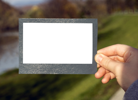 hand holds a gray frame on a landscape background