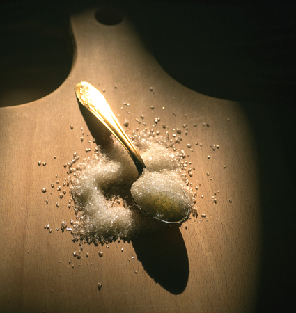 a spoon of sugar in a hand on a cutting board backgroundの写真素材