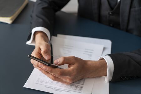 Top view of businessman hands using smartphone at blurred office table with contract and pen....