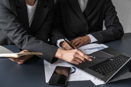 Hands of two businesswomen working together at office table and pointing at laptop screen. Concept of business partnershipの写真素材
