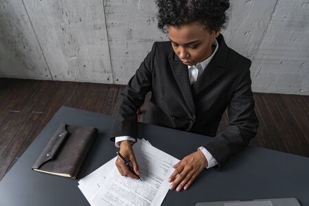 Top view of young African American woman working with documents or signing contract at loft office table. Concept of paperwork and managementの写真素材