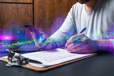 Double exposure of man signing contract with phone and forex graph hologram. Concept of financial...