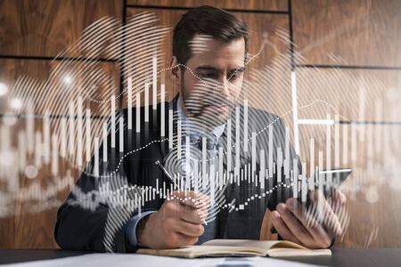 A businessman in office taking notes using phone and stock graph hologram. Multiexposure. Formal wear.の写真素材