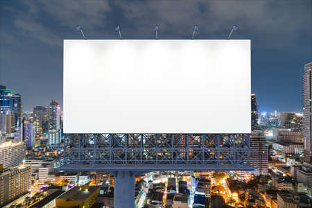 Blank white road billboard with Bangkok cityscape background at night time. Street advertising poster, mock up, 3D rendering. Front view. The concept of marketing communication to promote idea.の写真素材