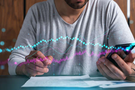 Double exposure of man signing contract with phone and forex graph hologram. Concept of financial...