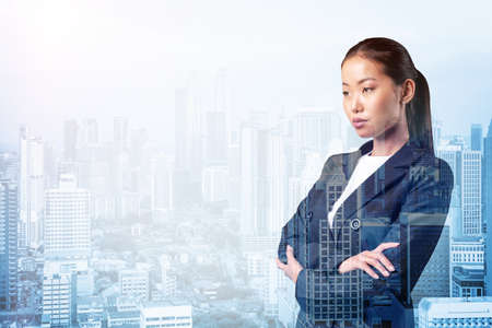 Prosperous Asian businesswoman in suit in crossed arms pose. Kuala Lumpur cityscape. The concept of woman in business. KL skyscrapers. Double exposure.の写真素材