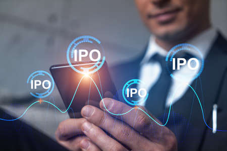 Analyst in office working with Smartphone, IPO hologram, typing phone. Double exposure.