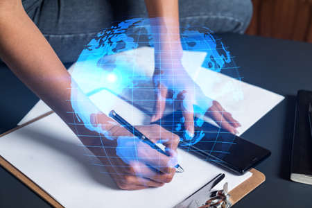 Businesswoman taking notes using smart-phone. World map hologram double exposure.