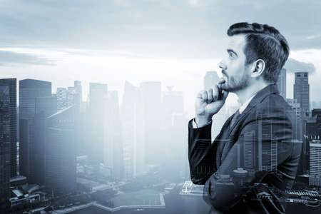 Young handsome businessman in suit with hand on chin thinking how to succeed, new career opportunities, MBA. Singapore on background. Double exposure.の写真素材