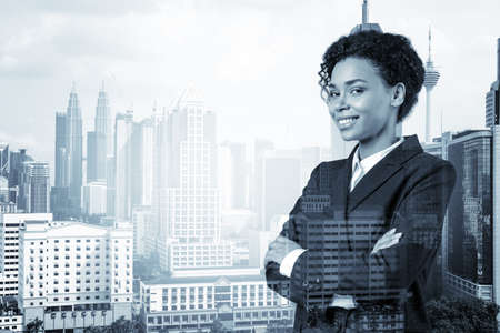 Smiling black African American business woman in suit in crossed arms pose. Kuala Lumpur cityscape....