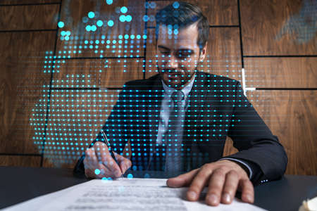 Businessman in office signs contract and world map hologram. Double exposure. Formal wear. International business connection.の写真素材