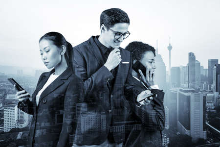 Group of successful smiling businesspeople in suits using smart phone and thinking how to tackle the...