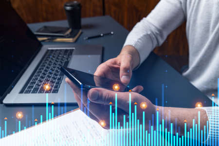 Man using phone. Hands typing smartphone. Double exposure with chart hologram. Close up. Financial...