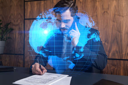 A man in office signing papers while talking mobile and planet earth hologram. Double exposure. Formal wear.の写真素材