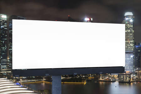 Blank white road billboard with cityscape background at night time.