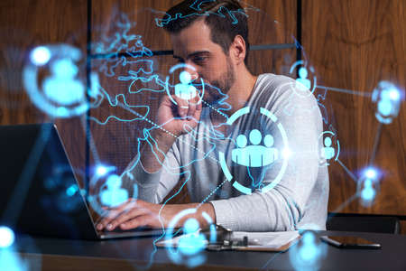 A serious Caucasian manager in casual wears, using laptop to develop a new network. Double exposure....