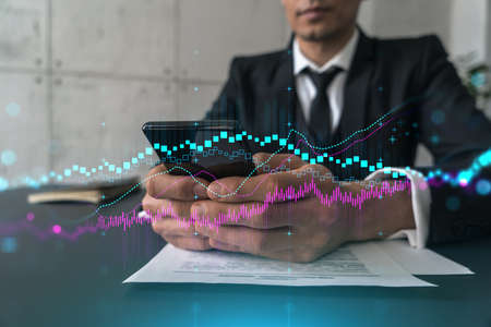 Trader in office working with Smartphone, FOREX graph hologram to analyze market behavior, typing...