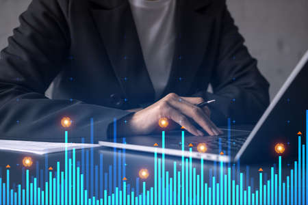 Businesswoman typing on computer in office. Fiancial graph hologram. Double exposure.