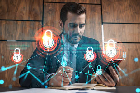 A man in office taking notes using phone and financial safety lock theme hologram. Multiexposure. Formal wear. Invest in stock market.の写真素材