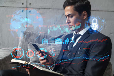 A man in office taking notes using phone and financial theme hologram. Multiexposure. Formal wear. Invest in stock market.の写真素材