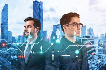 Two handsome young SMM specialists thinking about development of social media marketing strategy to achieve business goals. Hologram icons over Bangkok background.の写真素材