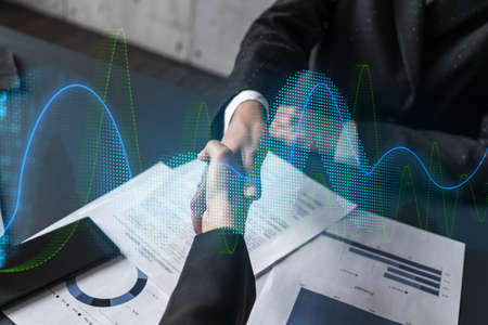 Double exposure of two businesspeople handshake and financial chart hologram drawing background....