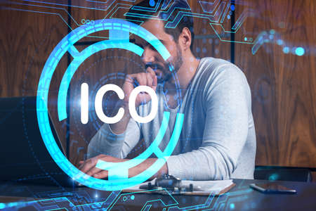 A serious caucasian analyst in casual wears, using laptop to proceed ICO project. Double exposure....