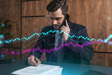 A man in office signing papers while talking phone and stock market graph and chart hologram. Double...