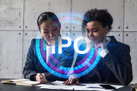 Two businesswomen work together in modern office on new project. Double exposure. Concept of success. IPO symbol icon.の写真素材