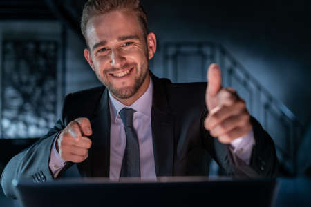 Portrait of happy businessman gesticulating wearing black suit, working late in the office. Office...