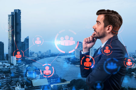 Handsome Caucasian HR director at international company is thinking about efficient strategy to recruit highly qualified specialists. Social media and marketing hologram icons over Bangkok background.の写真素材