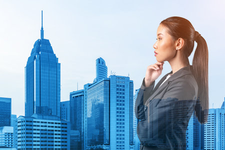 Attractive young Asian business woman in suit with hand on chin thinking how to succeed, new career opportunities, MBA. Kuala Lumpur on background. Double exposure.の写真素材