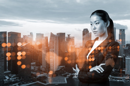 Attractive young Asian HR director at international company is thinking about recruitment of highly qualified specialists. Women in business concept. Social media hologram icons over Singapore.の写真素材