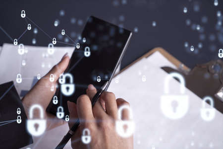 A businesswoman in formal wear checking the phone to sign the contract to prevent probability of risks in cyber security. Padlock Hologram icons over the working desk.の写真素材