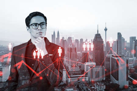 Handsome eastern HR director at international company thinking about efficient strategy to recruit highly qualified specialists. Social media and marketing hologram icons over Kuala Lumpur backgroundの写真素材