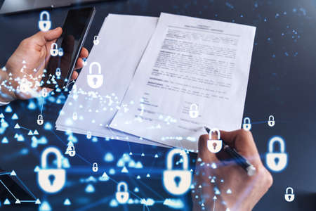 A businessman in formal wear signing the contract to prevent probability of risks in cyber security. Padlock Hologram icons over the working desk.の写真素材