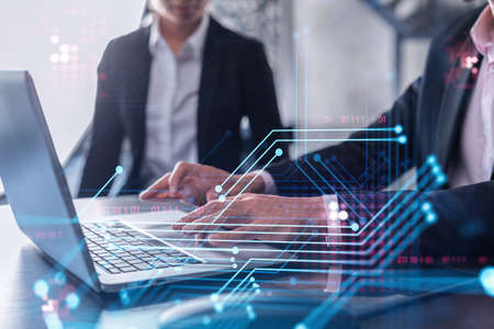 Two information technology specialist brainstorming on project to create a new approach to develop software to improve business service. Working with laptop. Tech hologram icons. Formal wear.の写真素材