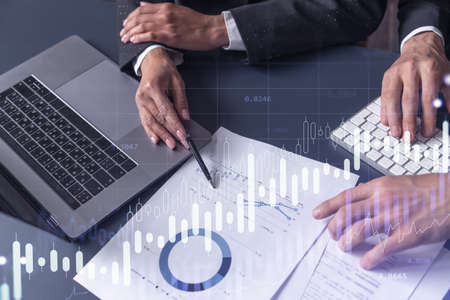 Two traders man and woman researching historic data to predict stock market behavior. Internet trading concept. Forex and financial hologram chart over the table with the documentsの写真素材