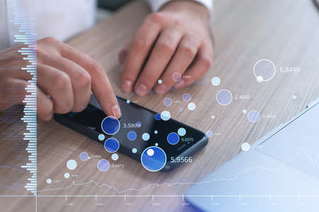 Trader holding in the hands a smart phone and researching stock market to proceed right investment...
