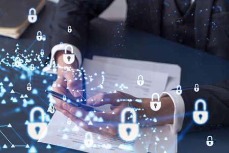 A businessman in formal wear reading the contract to prevent probability of risks in cyber security and checking details in the phone. Padlock Hologram icons over the working desk.の写真素材