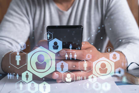 Hands of hr specialist browsing social networks in the Internet in smart phone to find the best candidates to hire international team. Concept of success. Media hologram icons.の写真素材