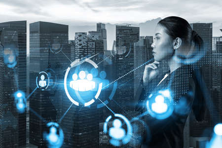 Attractive young Asian HR director at international company is thinking about recruitment of highly qualified specialists. Women in business concept. Social media hologram icons over Singapore.の写真素材